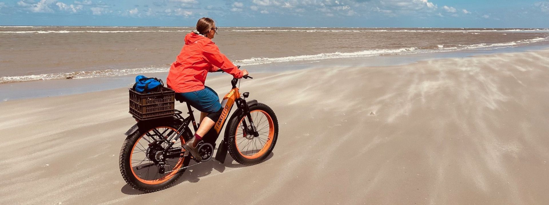 Frau radelt am Strand von Schiermonnikoog durch den wehendem Sand der weiten Natur